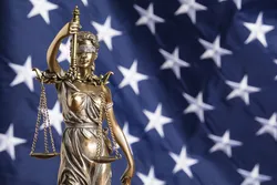 The statue of justice Themis or Justitia, the blindfolded goddess of justice against a flag of the United States of America