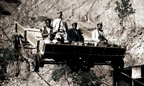 Three black and one white diamond miner on a transport vehicle in an open pit. Diamond mining in the 1800s, Kimberley, South Africa. Transport methods for miners in the open cast mine.